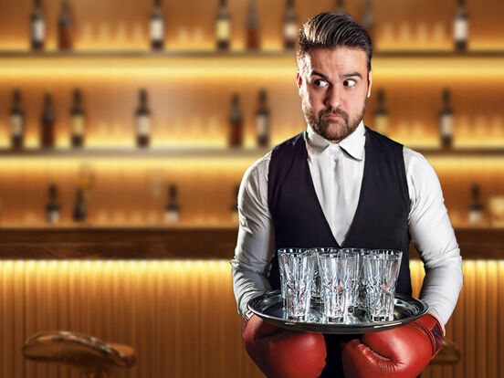 Barkeeper mit einem Tablett in der Hand, dem die Hände durch Boxhandschuhe gebunden sind
