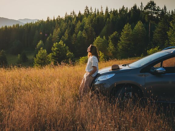 Eine Frau, die ihr Auto in einer Berglandschaft geparkt hat und sich an die Motorhaube anlehnt